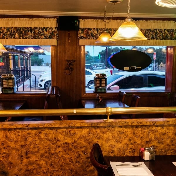 Cozy diner interior with wood paneling, patterned booths, and street views through large windows.