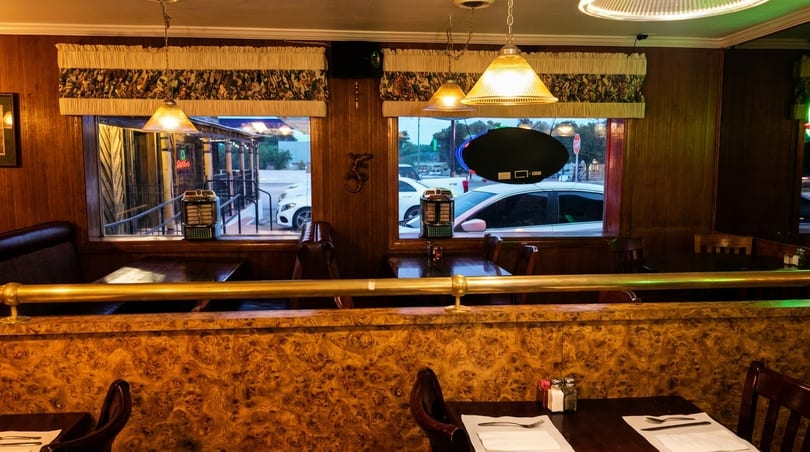 Cozy diner interior with wood paneling, patterned booths, and street views through large windows.
