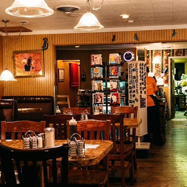 Cozy diner interior with wood paneling, hanging lights, and patrons dining at tables and booths.