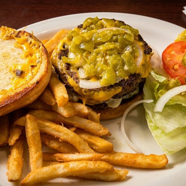Cheeseburger with green chiles, fries, and a side salad with tomatoes, pickles, and onions.