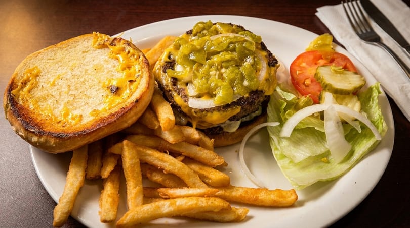 Cheeseburger with green chiles, fries, and a side salad with tomatoes, pickles, and onions.