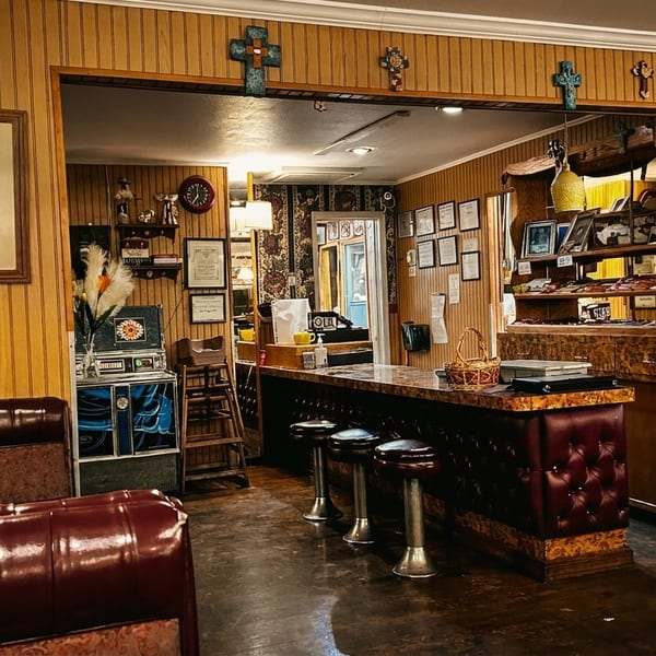 Cozy restaurant interior with wood paneling, a bar with stools, and framed pictures on the walls.