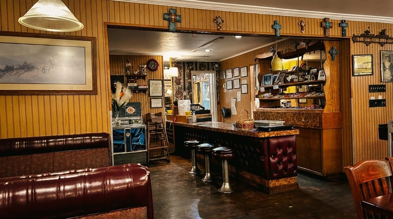 Cozy restaurant interior with wood paneling, a bar with stools, and framed pictures on the walls.