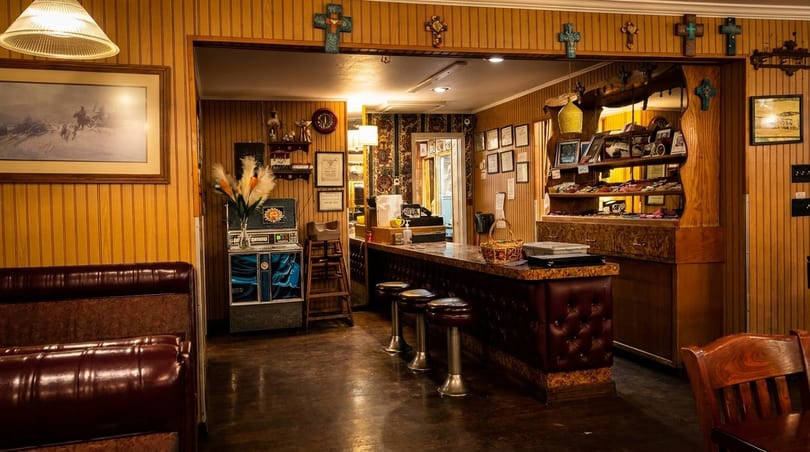 Cozy restaurant interior with wood paneling, a bar with stools, and framed artwork.