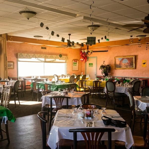 A restaurant dining room with tables set for a celebration, featuring green, yellow, and white tablecloths.