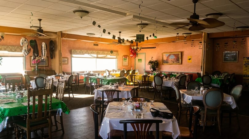 A restaurant dining room with tables set for a celebration, featuring green, yellow, and white tablecloths.