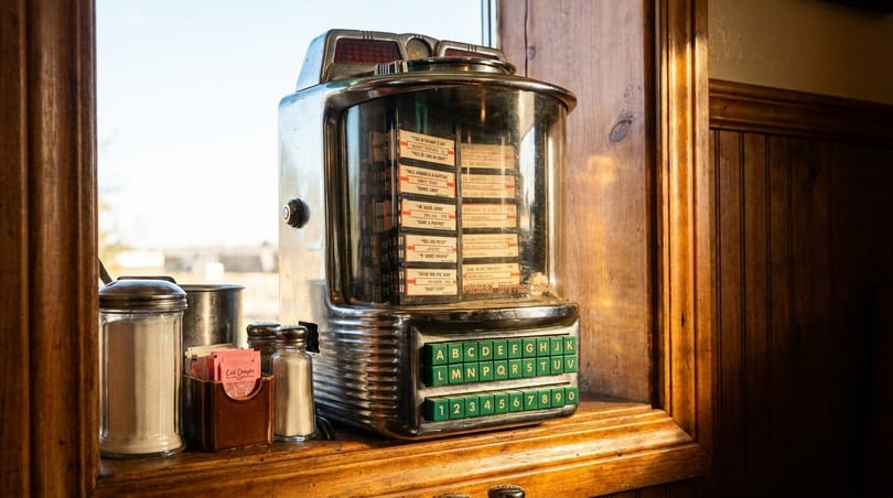 A vintage tabletop jukebox sits on a wooden window sill next to sugar and salt shakers.