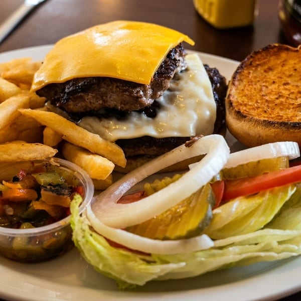 A double cheeseburger with melted cheese, fries, and a side salad with pickles and onions.