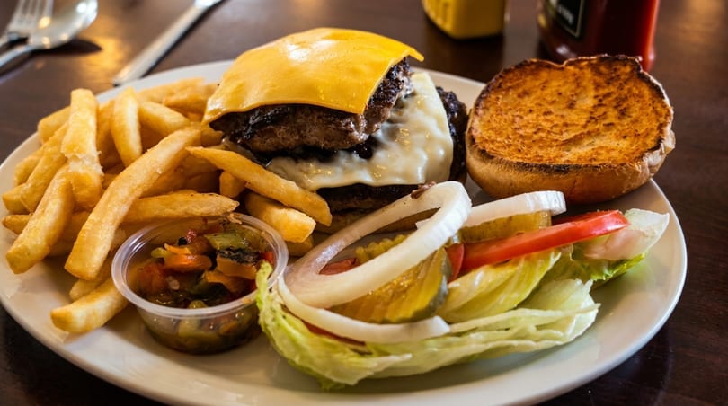 A double cheeseburger with melted cheese, fries, and a side salad with pickles and onions.